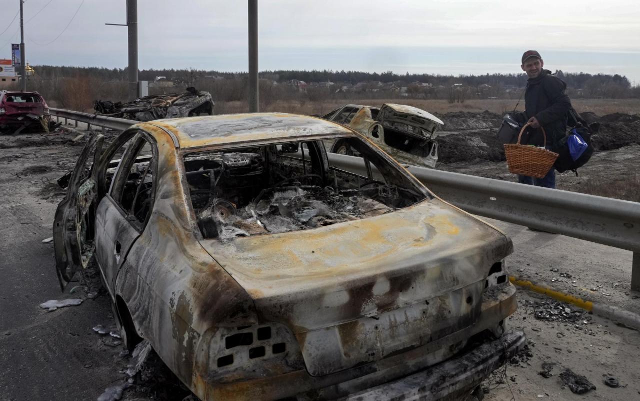 A resident passes by cars burnt in the Russian shellfire as he flees from his hometown on the road towards Kyiv, in the town of Irpin, northwest of Kyiv, Saturday, March 12, 2022. (AP Photo/Efrem Lukatsky)